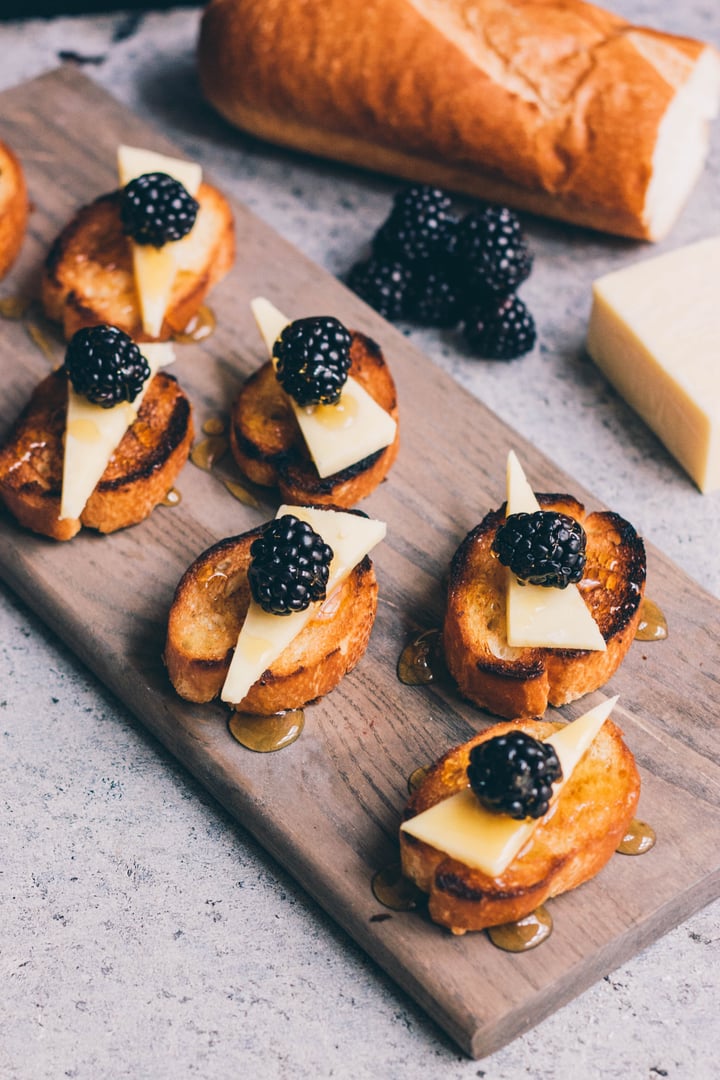 pieces of bruschetta  topped with cheese, honey, and blackberries 