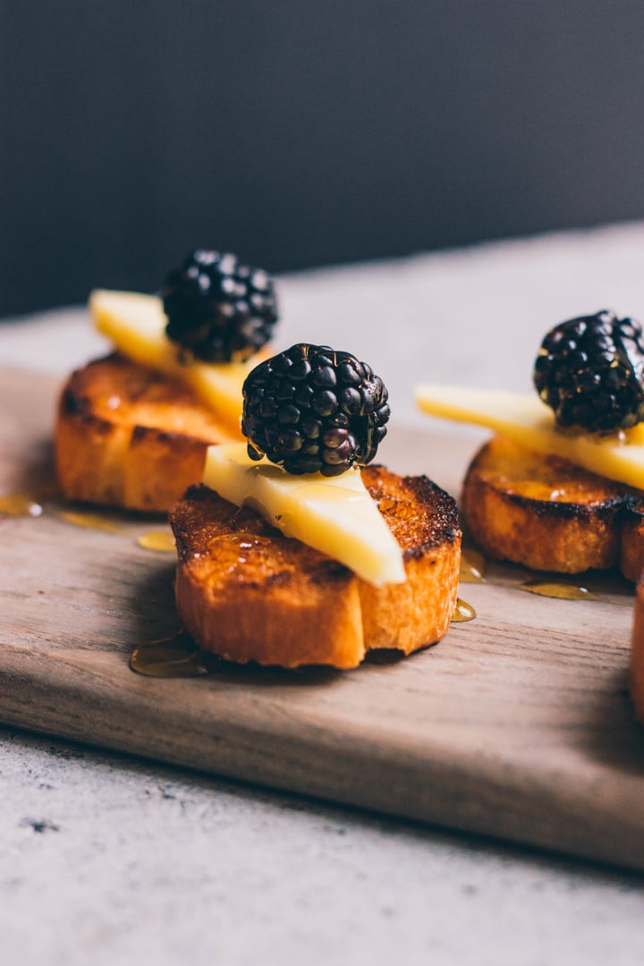 pieces of bruschetta  topped with cheese, honey, and blackberries 