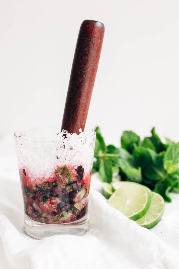 a muddler inside a glass with muddles blueberries and mint