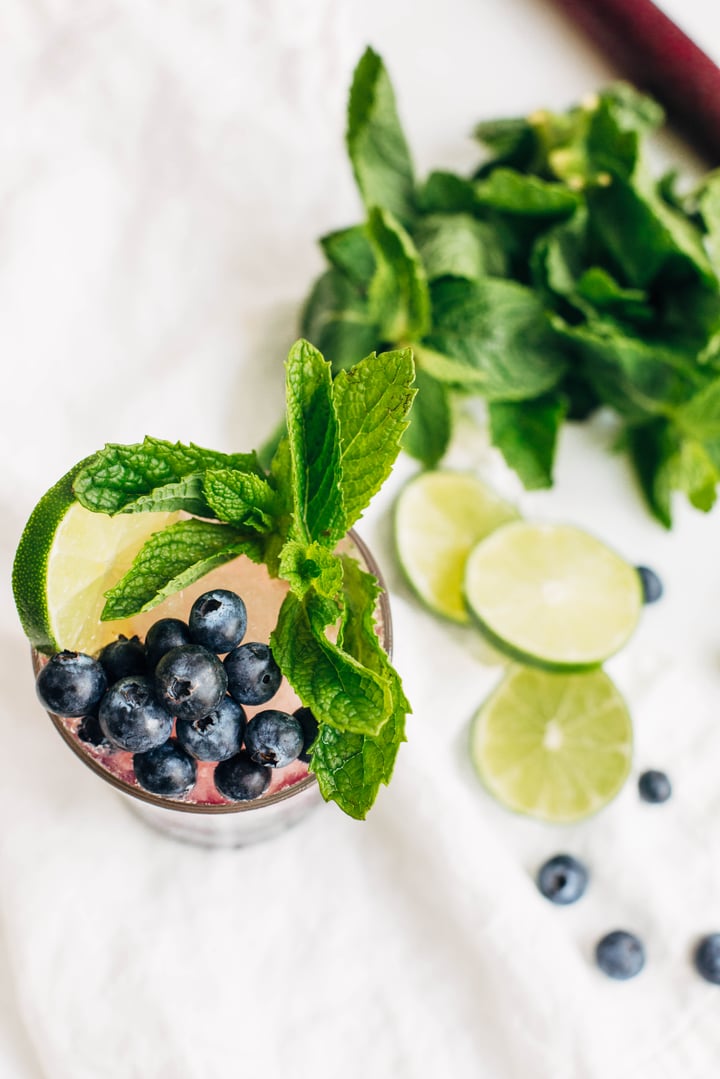 a blueberry and mint mojito garnished with a slice of lime, mint, and blueberries