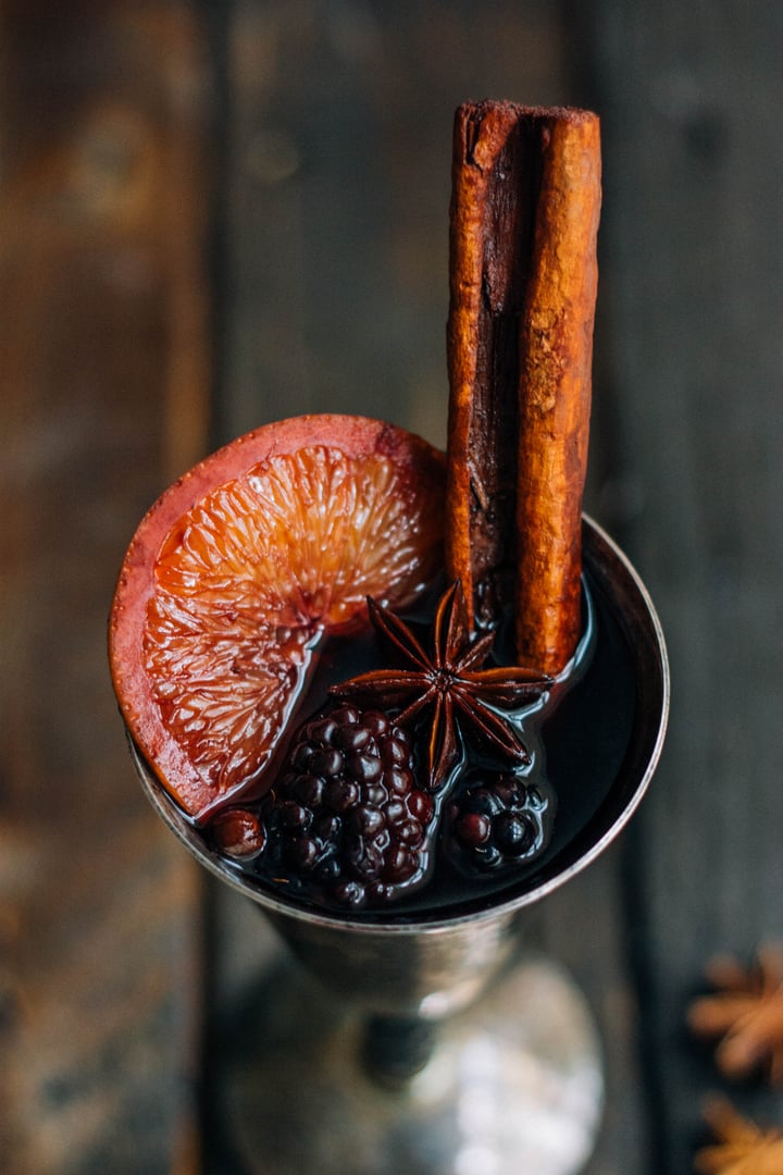 metal wine cup filled with wine and garnished with blackberries, a cinnamon stick, and a slice of an orange