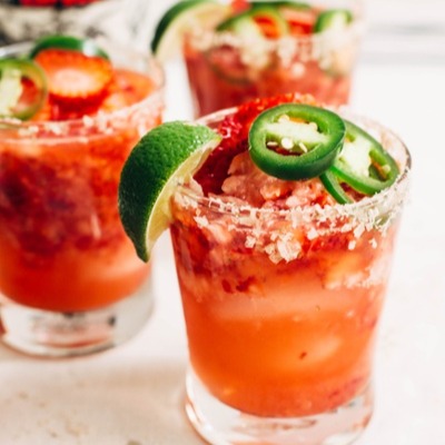 strawberry jalapeno margarita with a salted rim and garnished with a slice of lime, jalapenos, and a sliced strawberry