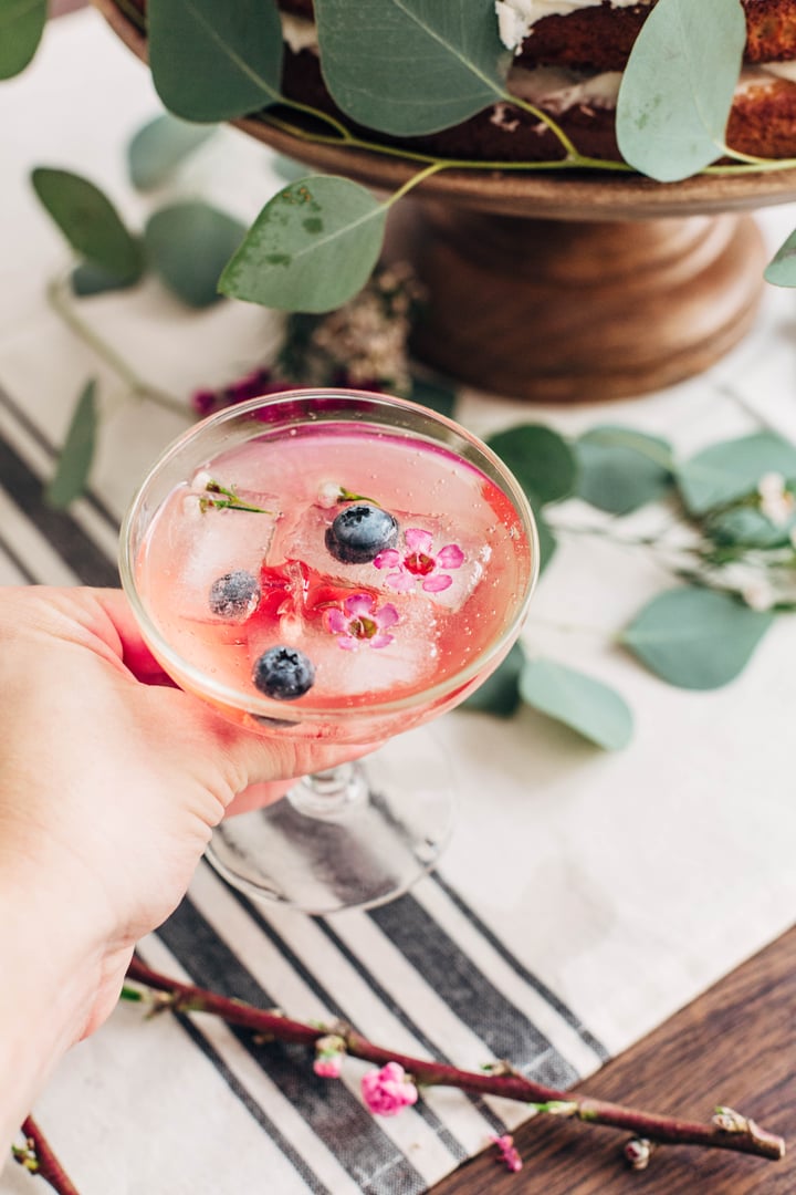 someone holding a glass of champagne with berry and flower edible ice cubes
