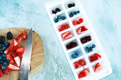 ice cube tray being filled in and adding berries to the water 