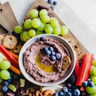 bowl of blueberry hummus surrounded by grapes and berries