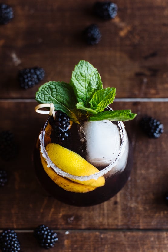 apple bourbon and blackberry sour topped with a lemon slice and a salted rim and and mint leaves