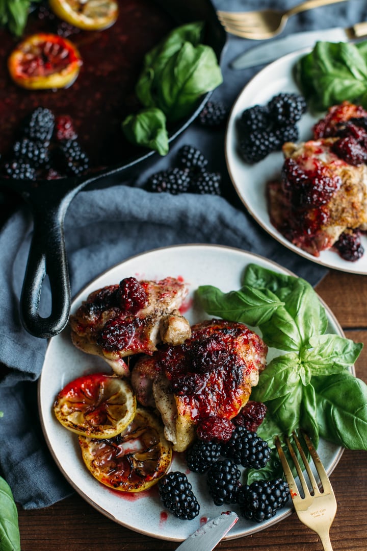 a plate with chicken thighs covered with blackberries with lemon slices on the side