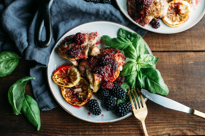 a plate with chicken thighs covered with blackberries and a side of sliced lemons and blackberries