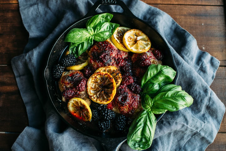 cast iron skillet with chicken thighs covered with blackberries and topped with slices of lemon