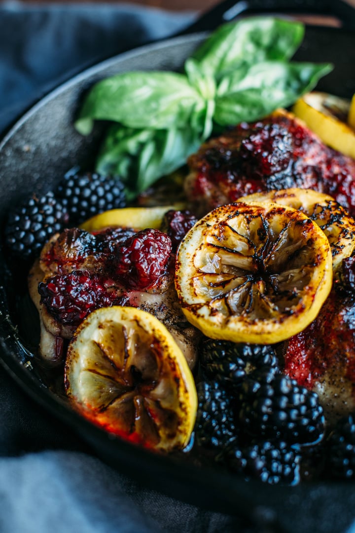 cast iron skillet with chicken thighs covered with blackberries and topped with slices of lemon