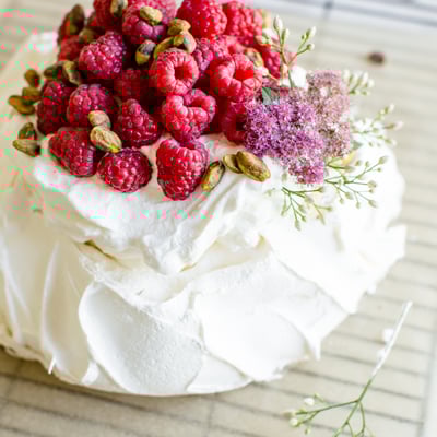 pistachio pavlova with whipped cream topped with raspberries and flowers