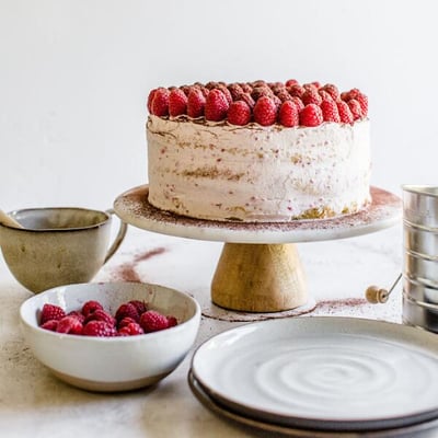 a round cake topped with raspberries on a cake stand