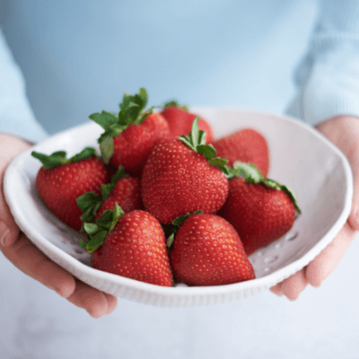 a close up picture of someone holding a bowl of strawberries