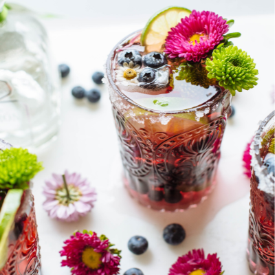 blueberry rose and tequila punch cocktail in a glass garnished with flowers and blueberries