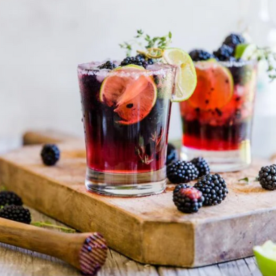 blackberry thyme margarita with a salted rim and topped with limes and blueberries