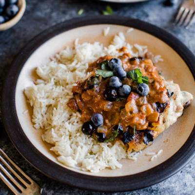 a plate with rice and chicken tikka masala laid on top with blueberries