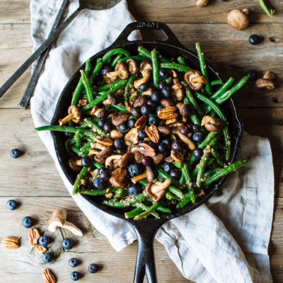 a mix of green beans, shiitake mushrooms, pecans, and blueberries in a cast iron skillet