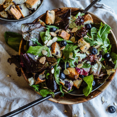 a salad with pieces of blueberry muffin croutons in a wooden bowl