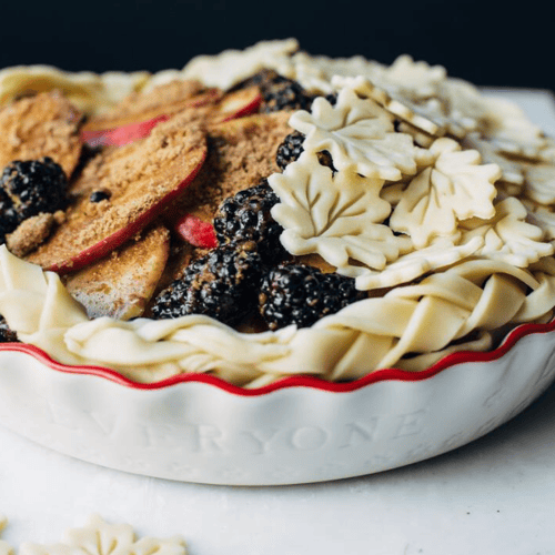 apple pie topped with blackberries and autumn leaves made out of the dough 