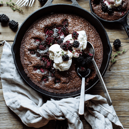 a brownie made in a cast iron skillet topped with blackberries and ice cream