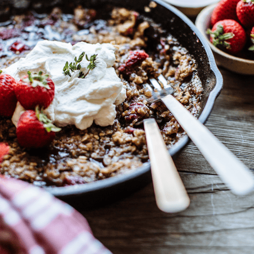 Oats and strawberries cooked in a cast iron skillet topped with whipped cream