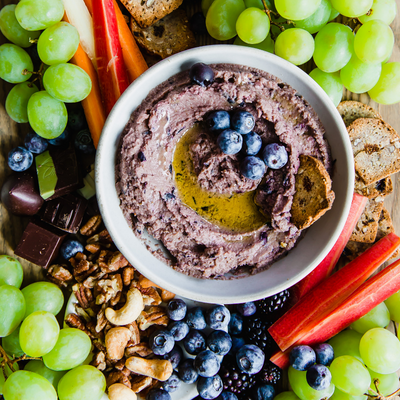 bowl of blueberry hummus surrounded by grapes and berries