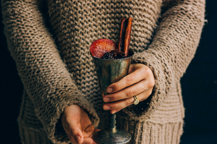 someone holding a metal wine cup filled with wine and garnished with blackberries, a cinnamon stick, and a slice of an orange