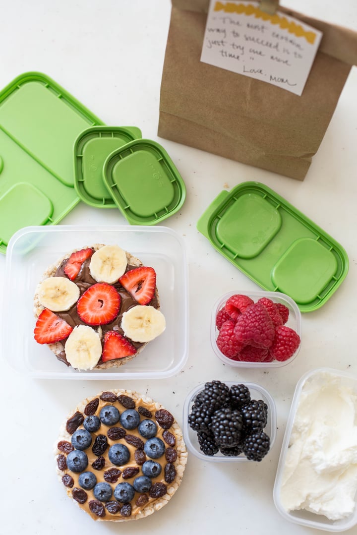 rice cake topped with blueberries, peanut butter, and raisins. and a rice cake topped with nutella, strawberries, and bananas with a side of raspberries and blackberries 