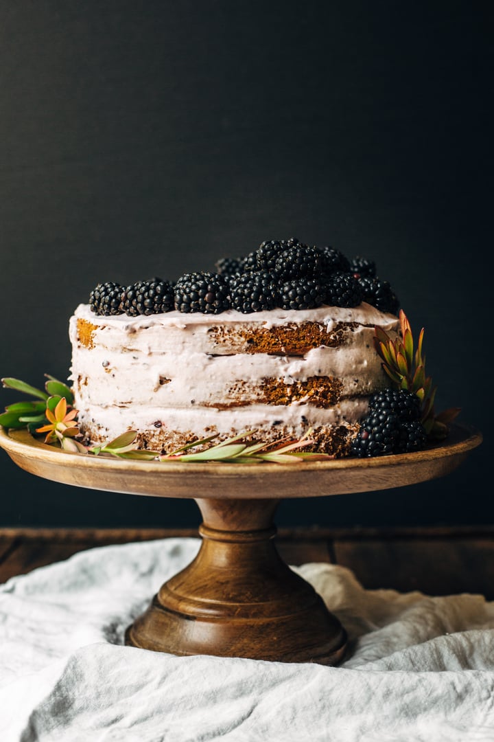 blackberry pumpkin spice cake topped with blackberries and frosting on a wooden cake stand