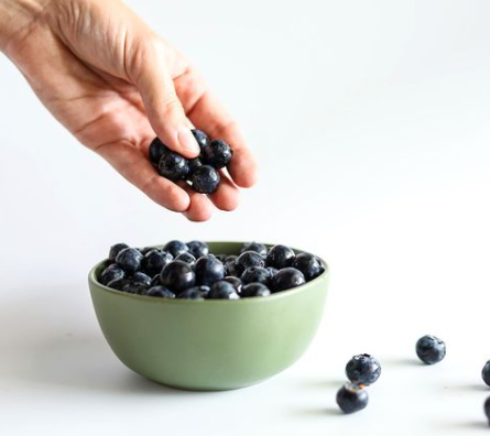 a hand picking up blueberries from a bowl 