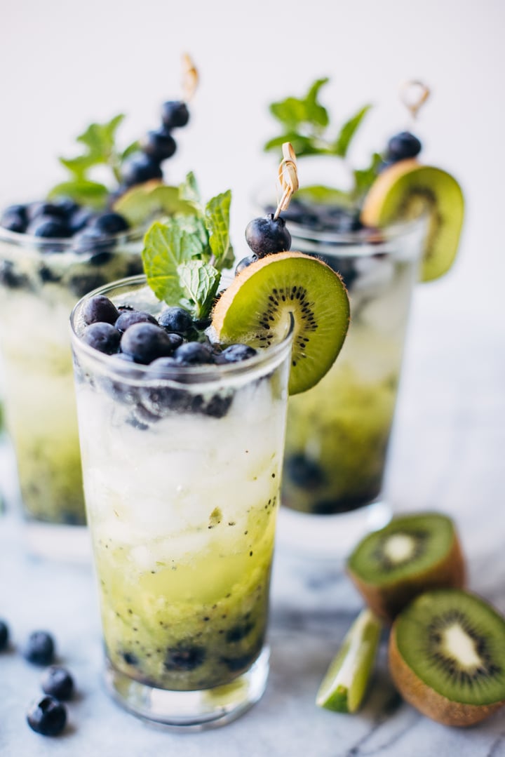 a blueberry and kiwi mojito in a glass garnished with blueberries, a slice of kiwi, and mint leaves