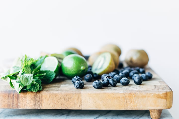 blueberries, kiwis, limes, and mint leaves on a cutting board