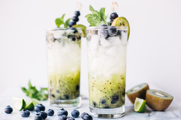 a blueberry and kiwi mojito in a glass garnished with blueberries, a slice of kiwi, and mint leaves