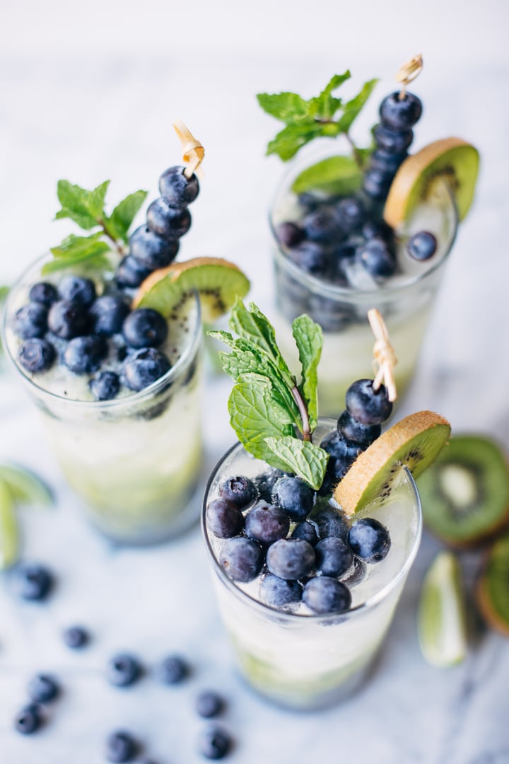 a blueberry and kiwi mojito in a glass garnished with blueberries, a slice of kiwi, and mint leaves