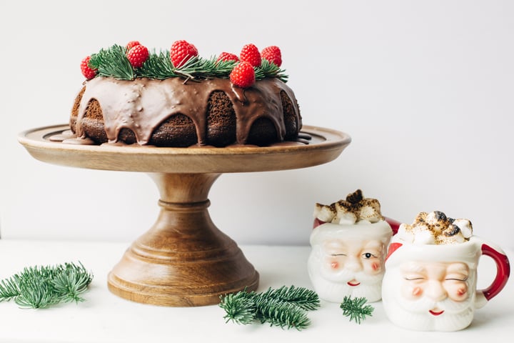 chocolate Bundt cake topped with raspberries and two santa clause mugs on the side