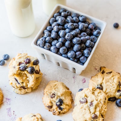 a clamshell of blueberries and blueberry and chocolate chip cookies surrounding it