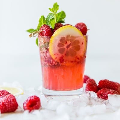 raspberry lemonade spritzer garnished with a slice of lemon, raspberries, and mint leaves