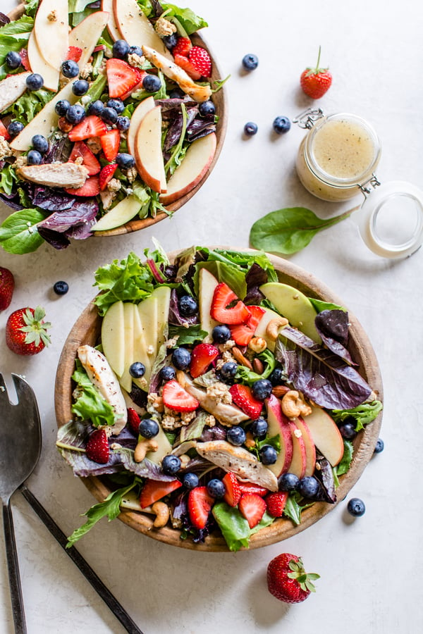 salad topped with apples, strawberries, blueberries, cashews, granola and chicken