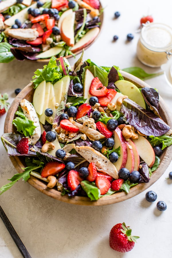 salad topped with apples, strawberries, blueberries, cashews, granola, and chicken