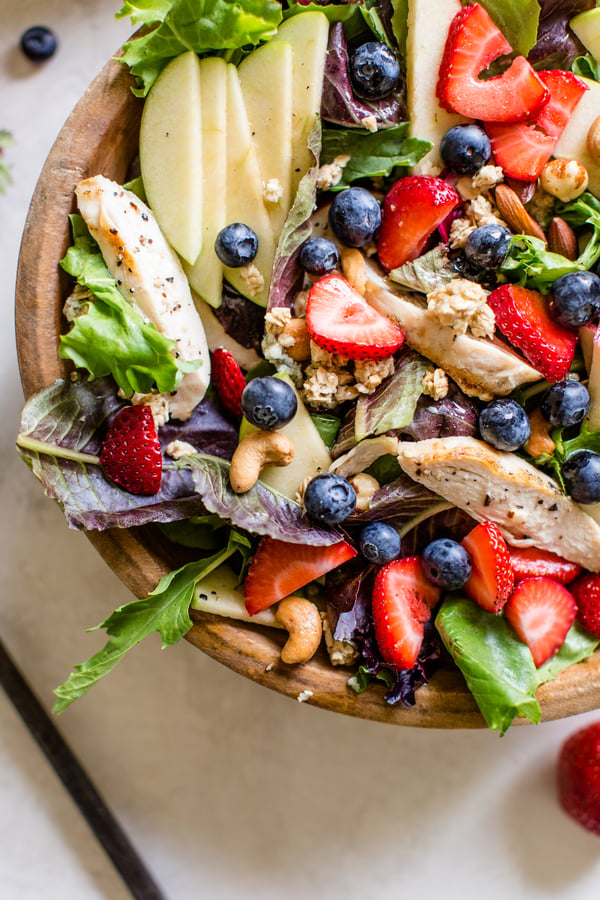 salad topped with apples, strawberries, blueberries, cashews, granola, and chicken