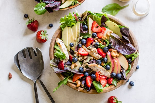 salad topped with apples, strawberries, blueberries, cashews, granola, and chicken