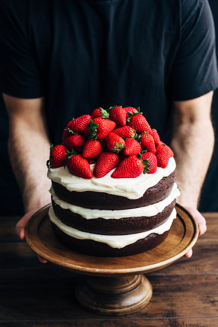 a close up of someone holding a chocolate cake topped with strawberries