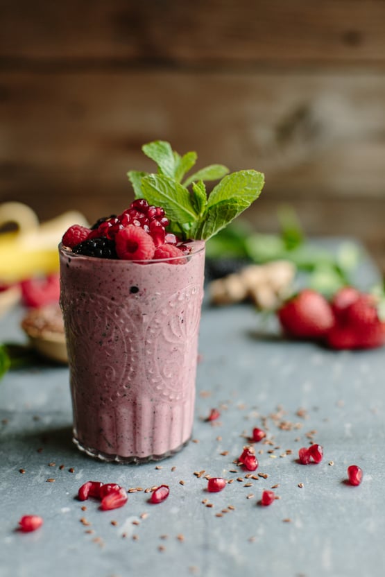 berry smoothie topped with berries, mint leaves, and pomegranate seeds