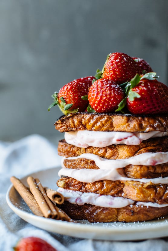 strawberries and cream stuffed French toast topped with whole strawberries and a side of cinnamon sticks