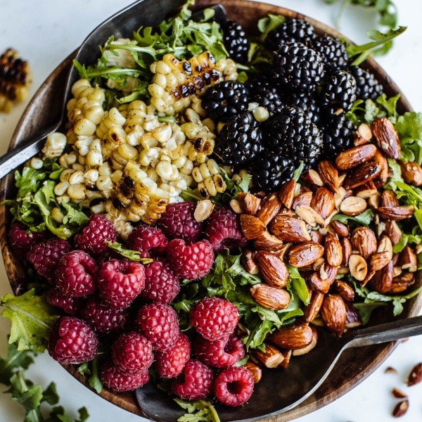 Salad topped with raspberries, corn, almonds, and blackberries