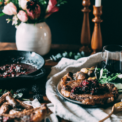 a table setting with a steak topped with blackberries on a plate