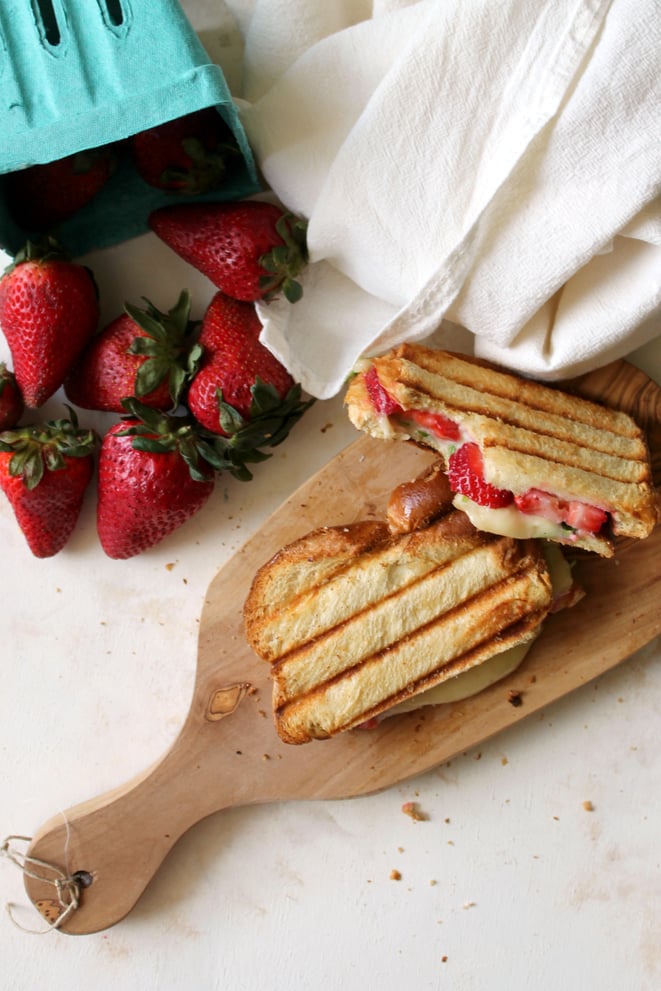 strawberry, brie, and arugula panini on a cutting board with strawberries on the side