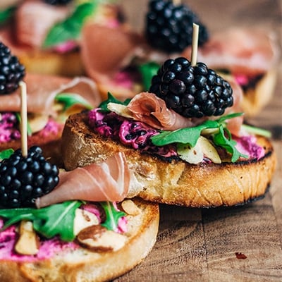 crostni topped with prosciutto, arugula, and blackberries