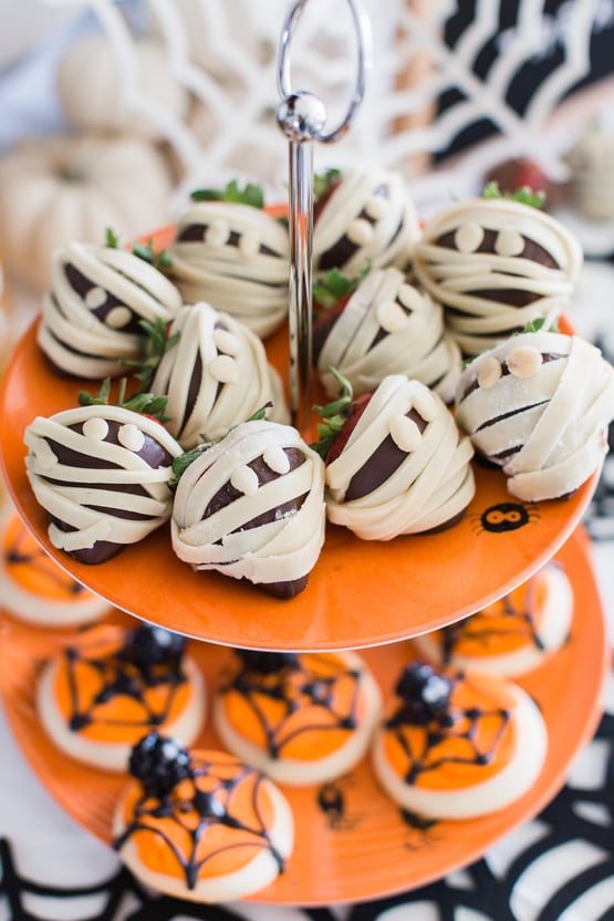 dessert tier with chocolate covered strawberries that look like mummies and orange sugar cookies with a spider design