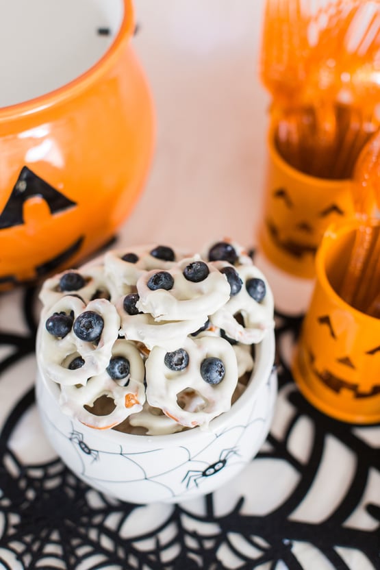 a cauldron filled with white chocolate dipped pretzels with blueberries made to look like eyes on each of them